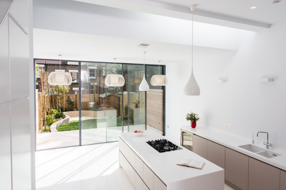 Medium sized contemporary l-shaped open plan kitchen in London with an integrated sink, flat-panel cabinets, white cabinets, composite countertops, black appliances, ceramic flooring, an island, white floors and white worktops.