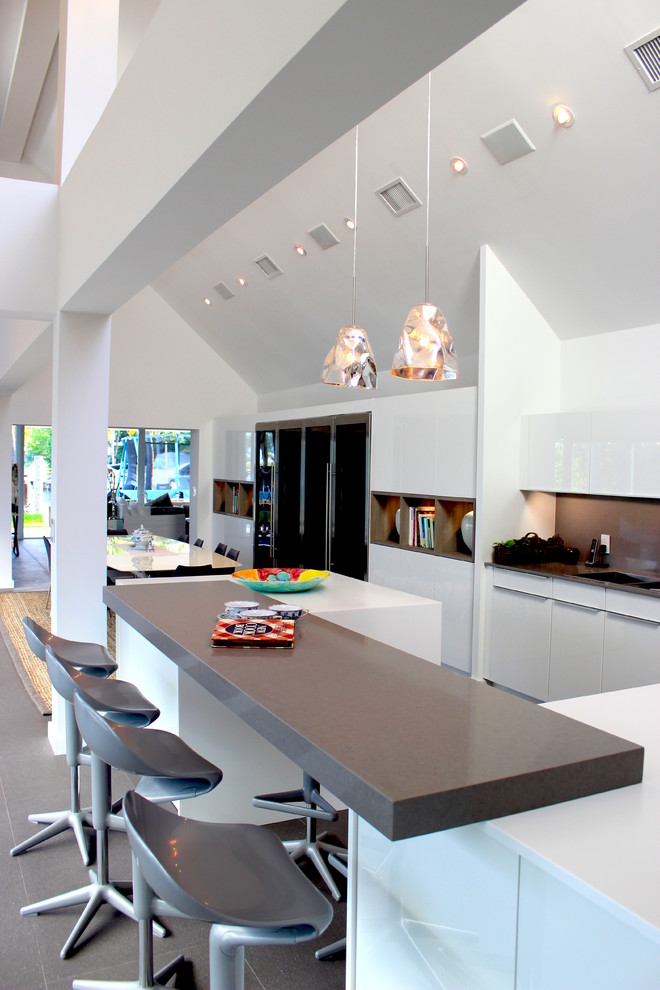 Источник вдохновения для домашнего уюта: большая угловая кухня в современном стиле с обеденным столом, плоскими фасадами, белыми фасадами, серым фартуком и техникой из нержавеющей стали