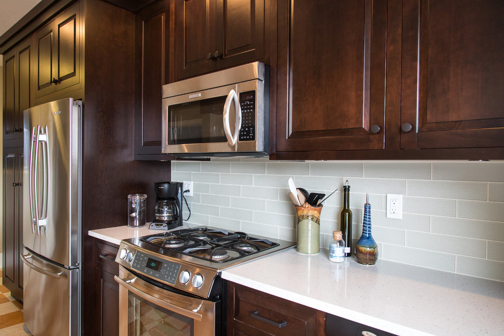 Modern inredning av ett mellanstort kök, med en undermonterad diskho, luckor med upphöjd panel, skåp i mörkt trä, bänkskiva i kvarts, grönt stänkskydd, stänkskydd i glaskakel, rostfria vitvaror, linoleumgolv och en köksö