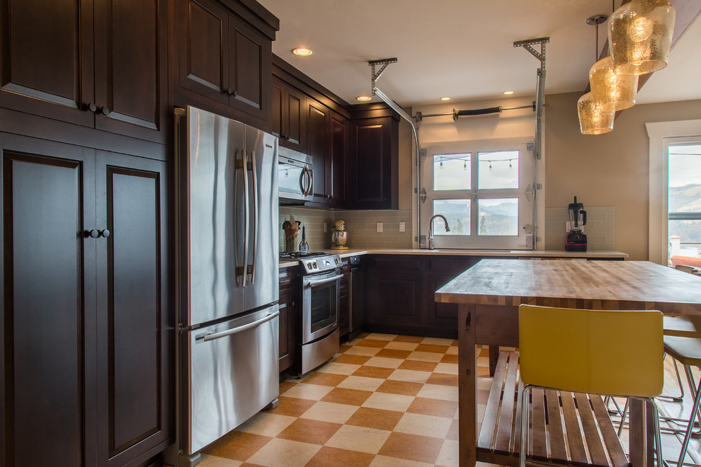 Example of a mid-sized trendy l-shaped linoleum floor open concept kitchen design in Portland with dark wood cabinets, glass tile backsplash, stainless steel appliances, an island, an undermount sink, raised-panel cabinets, quartz countertops and green backsplash