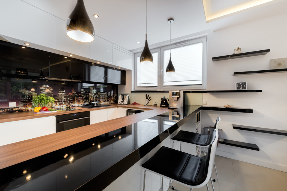 Medium sized modern u-shaped kitchen/diner in New York with a double-bowl sink, flat-panel cabinets, white cabinets, wood worktops, multi-coloured splashback, black appliances, porcelain flooring, a breakfast bar and beige floors.