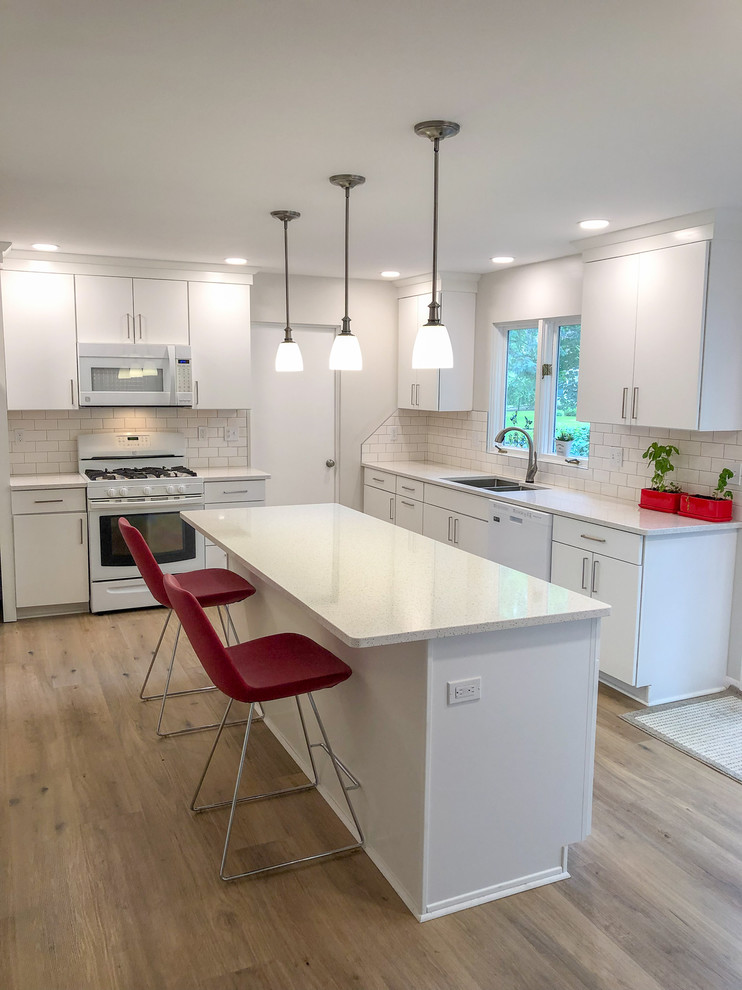 Inspiration for a mid-sized modern vinyl floor and brown floor kitchen remodel in Other with an undermount sink, flat-panel cabinets, white cabinets, quartz countertops, white backsplash, subway tile backsplash, white appliances, an island and white countertops