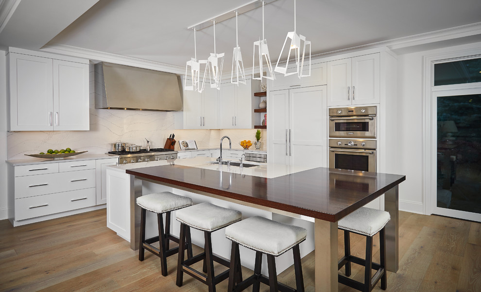 Kitchen - large transitional l-shaped medium tone wood floor kitchen idea in Grand Rapids with an undermount sink, white cabinets, wood countertops, white backsplash, stainless steel appliances, an island and shaker cabinets