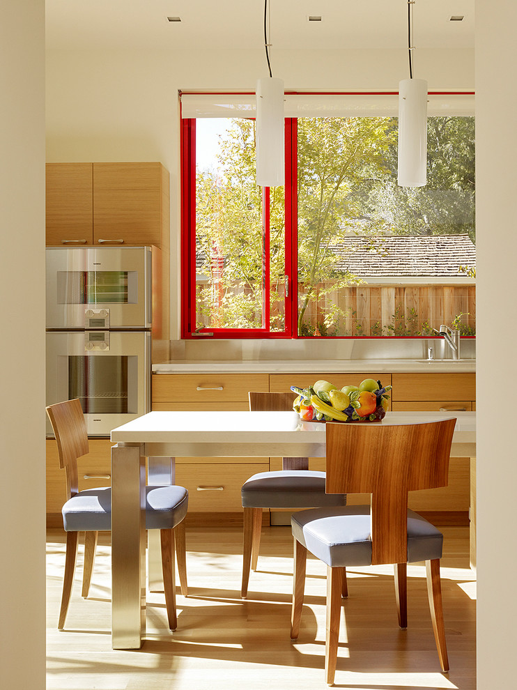 Стильный дизайн: кухня среднего размера в современном стиле с плоскими фасадами, светлыми деревянными фасадами, светлым паркетным полом, обеденным столом и техникой из нержавеющей стали - последний тренд