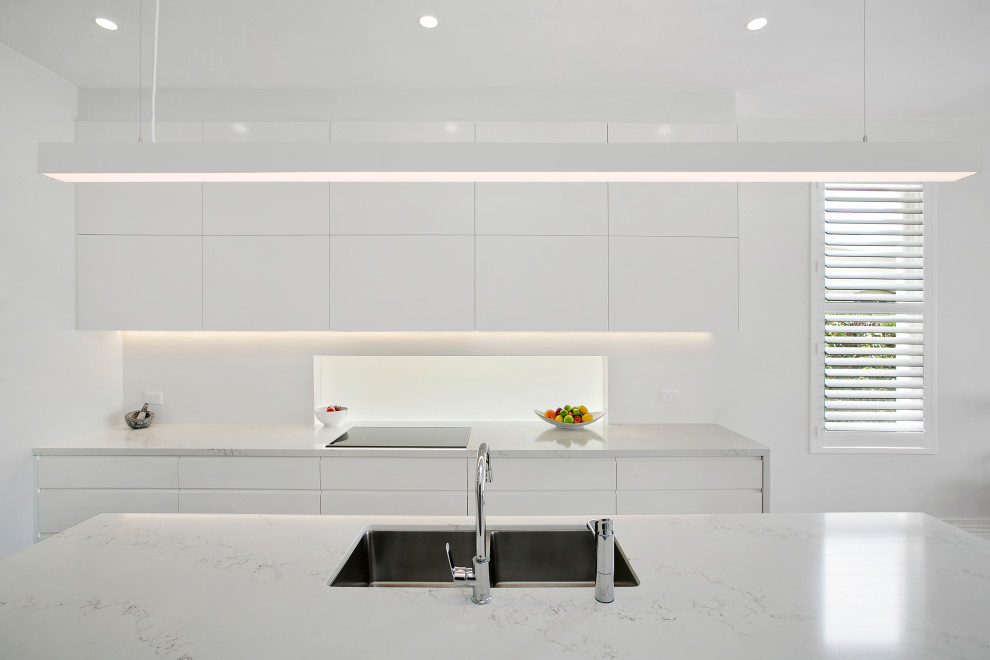 Photo of a beach style kitchen in Sydney with white cabinets, engineered stone countertops, white splashback, medium hardwood flooring, an island and white worktops.