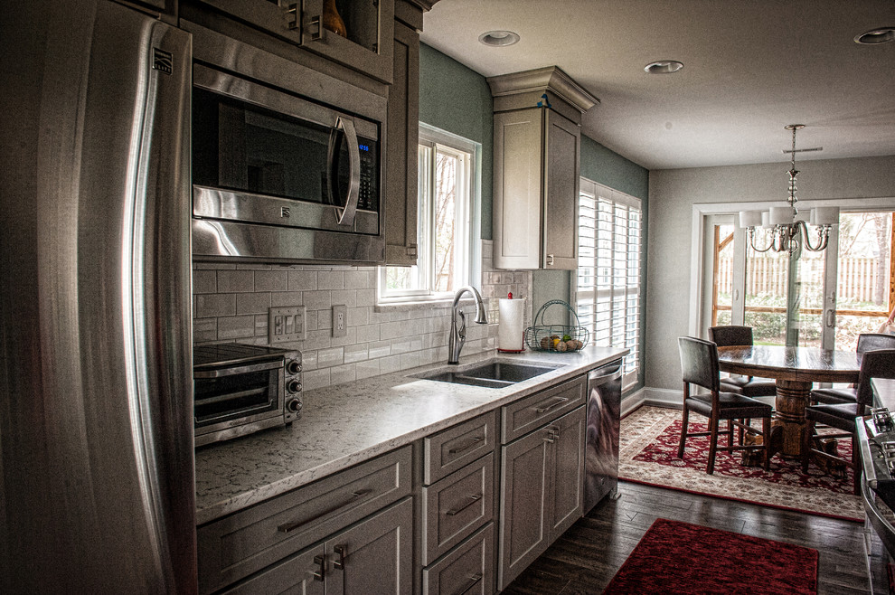 Klassisk inredning av ett mellanstort kök, med en dubbel diskho, skåp i shakerstil, grå skåp, marmorbänkskiva, vitt stänkskydd, stänkskydd i tunnelbanekakel, rostfria vitvaror och mörkt trägolv