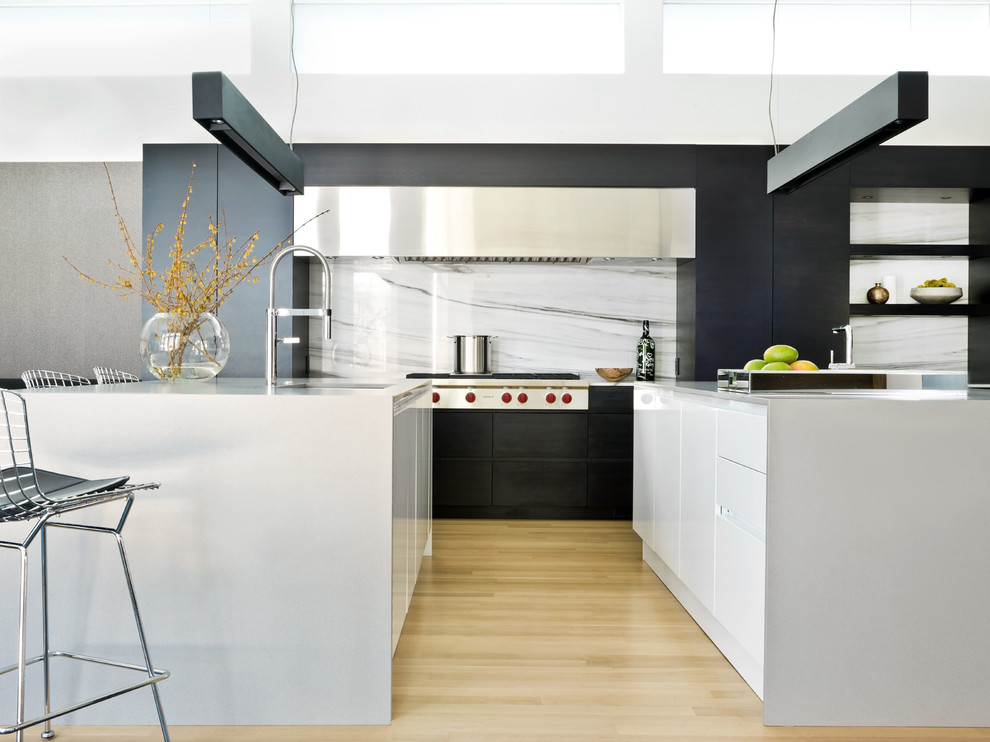 Photo of a scandi kitchen in Chicago with a submerged sink, flat-panel cabinets, white cabinets, white splashback, stainless steel appliances and light hardwood flooring.
