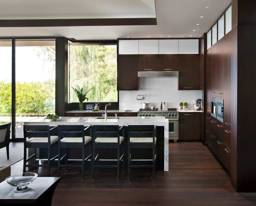 Medium sized contemporary l-shaped kitchen/diner in Detroit with a submerged sink, flat-panel cabinets, dark wood cabinets, marble worktops, white splashback, stainless steel appliances, medium hardwood flooring and an island.