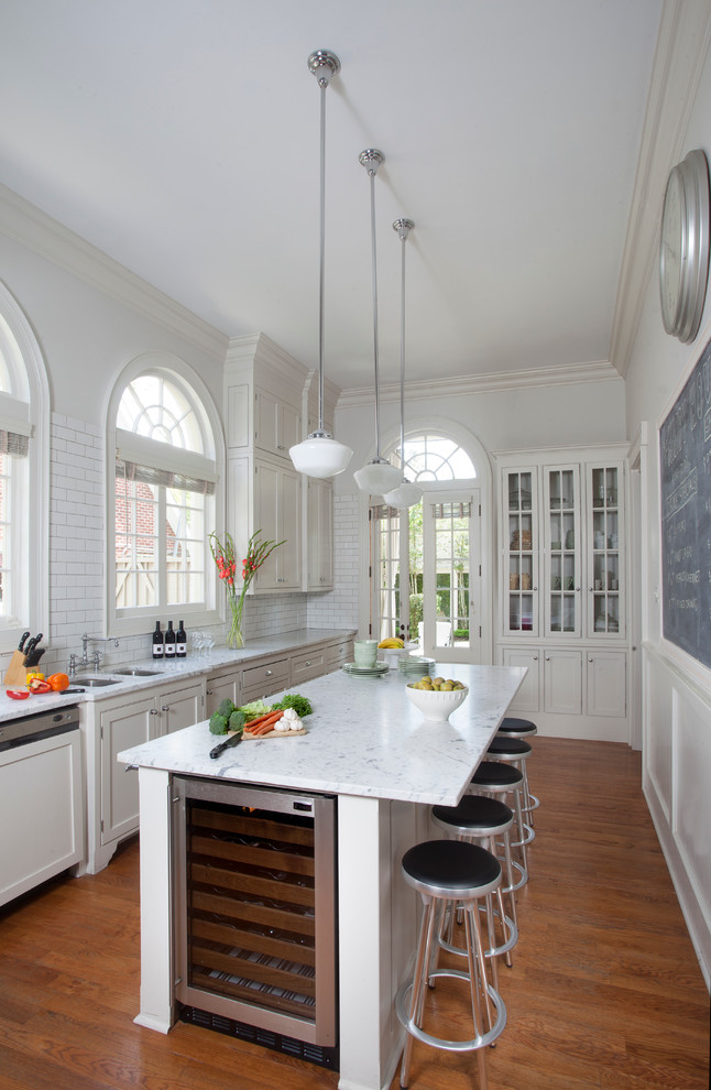 Geschlossene Klassische Küche mit Schrankfronten im Shaker-Stil, weißen Schränken, Küchenrückwand in Weiß, Rückwand aus Metrofliesen, braunem Holzboden und Kücheninsel in New Orleans