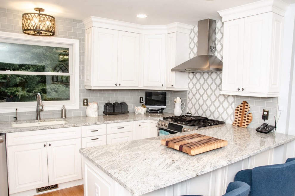 Inredning av ett klassiskt grå grått kök, med en undermonterad diskho, luckor med infälld panel, vita skåp, granitbänkskiva, flerfärgad stänkskydd, stänkskydd i porslinskakel, rostfria vitvaror, ljust trägolv, en halv köksö och brunt golv