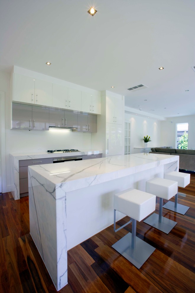 Bild på ett stort funkis kök, med en undermonterad diskho, släta luckor, vita skåp, marmorbänkskiva, vitt stänkskydd, glaspanel som stänkskydd, rostfria vitvaror, mellanmörkt trägolv och en köksö