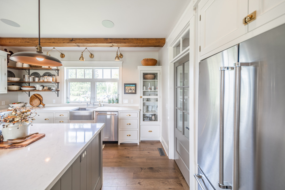 Example of a large classic l-shaped medium tone wood floor and brown floor eat-in kitchen design with a farmhouse sink, flat-panel cabinets, white cabinets, quartz countertops, beige backsplash, stainless steel appliances, an island and white countertops