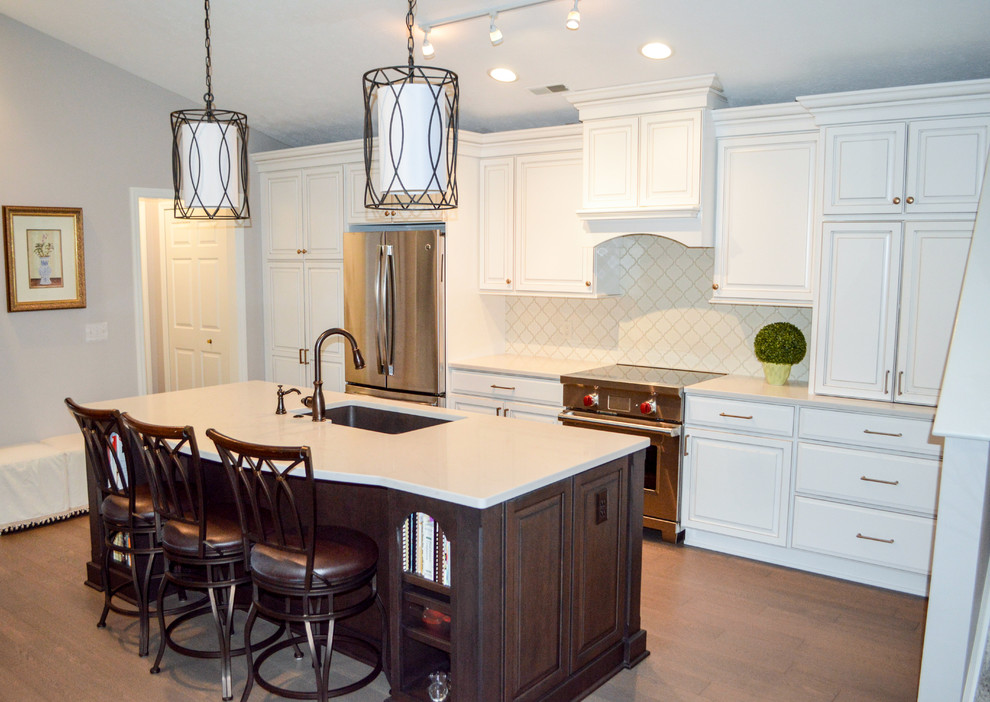 Inredning av ett klassiskt litet vit linjärt vitt kök med öppen planlösning, med en undermonterad diskho, luckor med upphöjd panel, vita skåp, bänkskiva i kvarts, vitt stänkskydd, stänkskydd i porslinskakel, rostfria vitvaror, mellanmörkt trägolv, en köksö och brunt golv