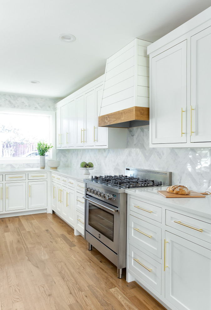 Foto de cocinas en L actual, grande, abierta, con fregadero bajoencimera, armarios estilo shaker, puertas de armario blancas, encimera de cuarzo compacto, salpicadero blanco, salpicadero de mármol, electrodomésticos de acero inoxidable, suelo de madera clara, una isla, suelo marrón y encimeras blancas