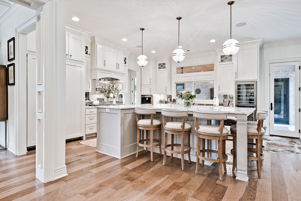 Exempel på ett stort klassiskt vit vitt kök och matrum, med luckor med infälld panel, vita skåp, bänkskiva i kvartsit, spegel som stänkskydd, rostfria vitvaror, en köksö och ljust trägolv