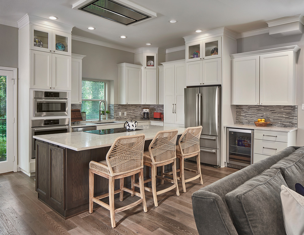 Example of a transitional l-shaped light wood floor open concept kitchen design in Dallas with an undermount sink, shaker cabinets, white cabinets, multicolored backsplash, matchstick tile backsplash, stainless steel appliances, an island and white countertops