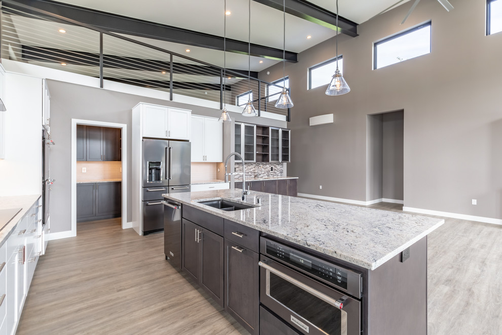 Example of a minimalist gray floor kitchen design in Seattle with shaker cabinets, gray cabinets, granite countertops, gray backsplash, stainless steel appliances, an island and white countertops