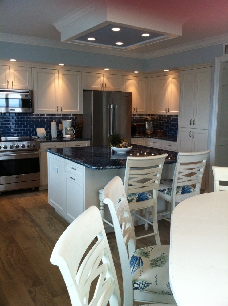 Example of a large beach style u-shaped porcelain tile enclosed kitchen design in Tampa with an undermount sink, recessed-panel cabinets, white cabinets, granite countertops, blue backsplash, glass tile backsplash, stainless steel appliances and an island