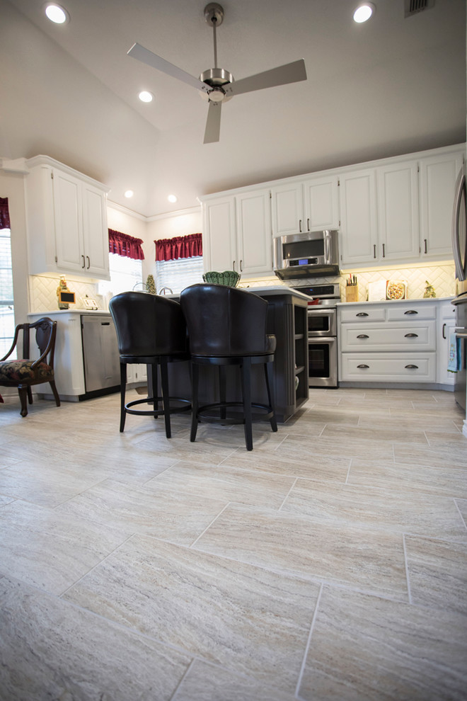 Example of a mid-sized classic l-shaped porcelain tile and gray floor eat-in kitchen design in Dallas with an undermount sink, raised-panel cabinets, white cabinets, quartz countertops, white backsplash, subway tile backsplash, stainless steel appliances and an island