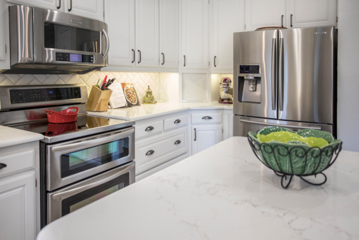 Inredning av ett klassiskt mellanstort kök, med en undermonterad diskho, luckor med upphöjd panel, vita skåp, bänkskiva i kvarts, vitt stänkskydd, stänkskydd i tunnelbanekakel, rostfria vitvaror, klinkergolv i porslin, en köksö och grått golv