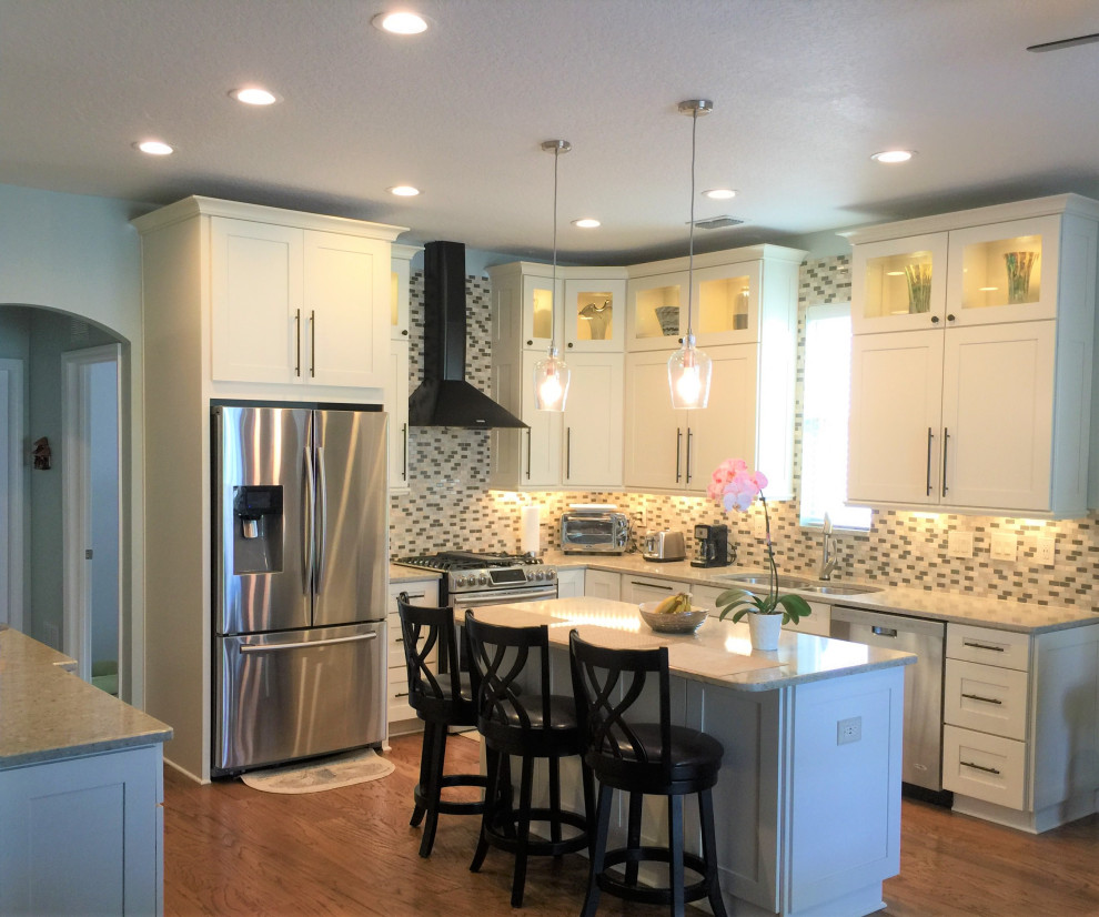 Inspiration for a mid-sized coastal u-shaped medium tone wood floor and brown floor open concept kitchen remodel in Orlando with an undermount sink, white cabinets, quartzite countertops, multicolored backsplash, mosaic tile backsplash, stainless steel appliances, an island and beige countertops