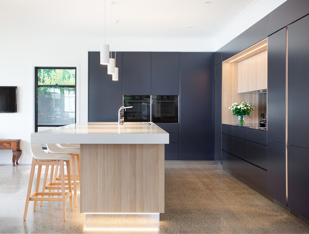 Large trendy l-shaped concrete floor and multicolored floor kitchen pantry photo in Brisbane with a double-bowl sink, flat-panel cabinets, light wood cabinets, quartz countertops, mirror backsplash, black appliances, an island and white countertops