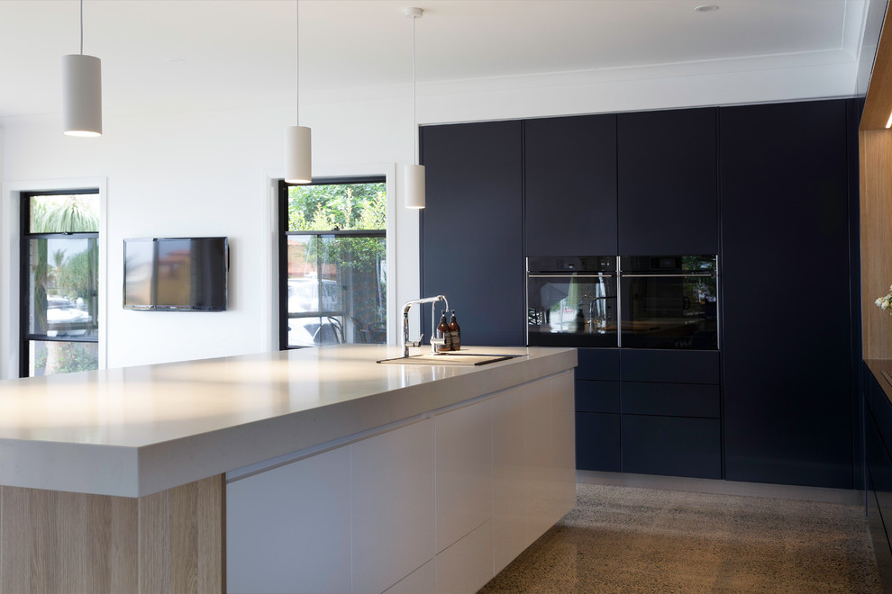 Design ideas for a large contemporary l-shaped kitchen pantry in Brisbane with a double-bowl sink, flat-panel cabinets, light wood cabinets, engineered stone countertops, mirror splashback, black appliances, concrete flooring, an island, multi-coloured floors and white worktops.