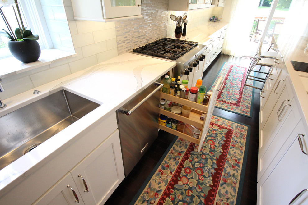 Zweizeilige, Mittelgroße Moderne Wohnküche mit Waschbecken, flächenbündigen Schrankfronten, weißen Schränken, Küchenrückwand in Weiß, Küchengeräten aus Edelstahl, dunklem Holzboden und Kücheninsel in Detroit