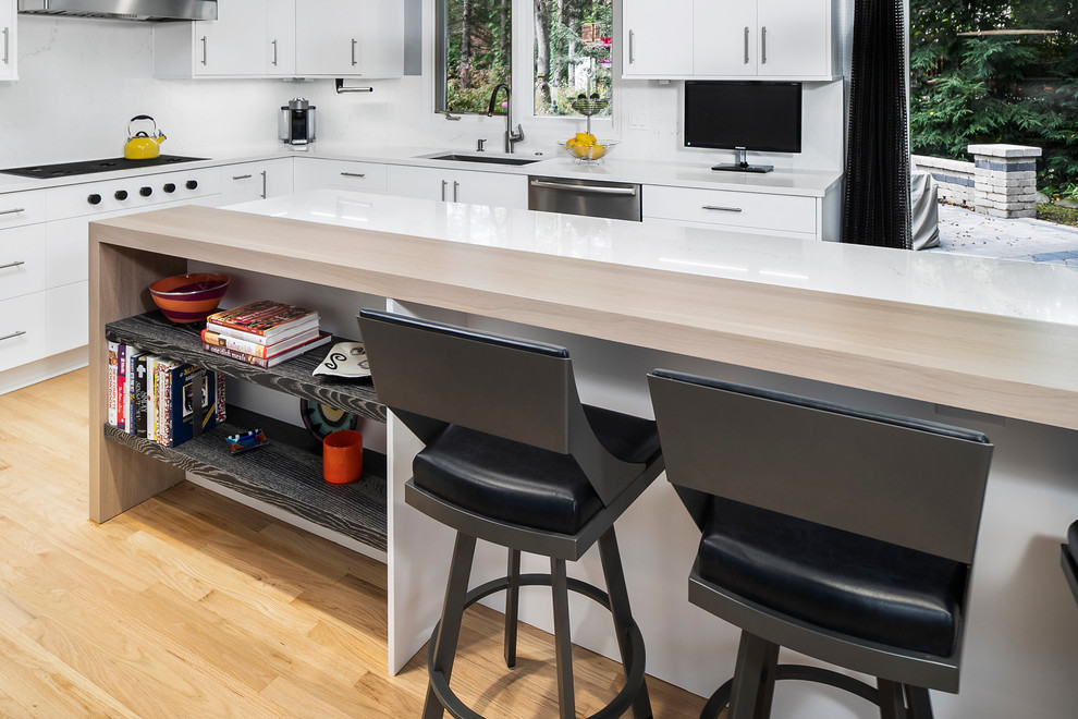 デトロイトにある高級な広いコンテンポラリースタイルのおしゃれなキッチン (アンダーカウンターシンク、フラットパネル扉のキャビネット、白いキャビネット、クオーツストーンカウンター、白いキッチンパネル、石スラブのキッチンパネル、シルバーの調理設備、無垢フローリング、茶色い床、白いキッチンカウンター) の写真