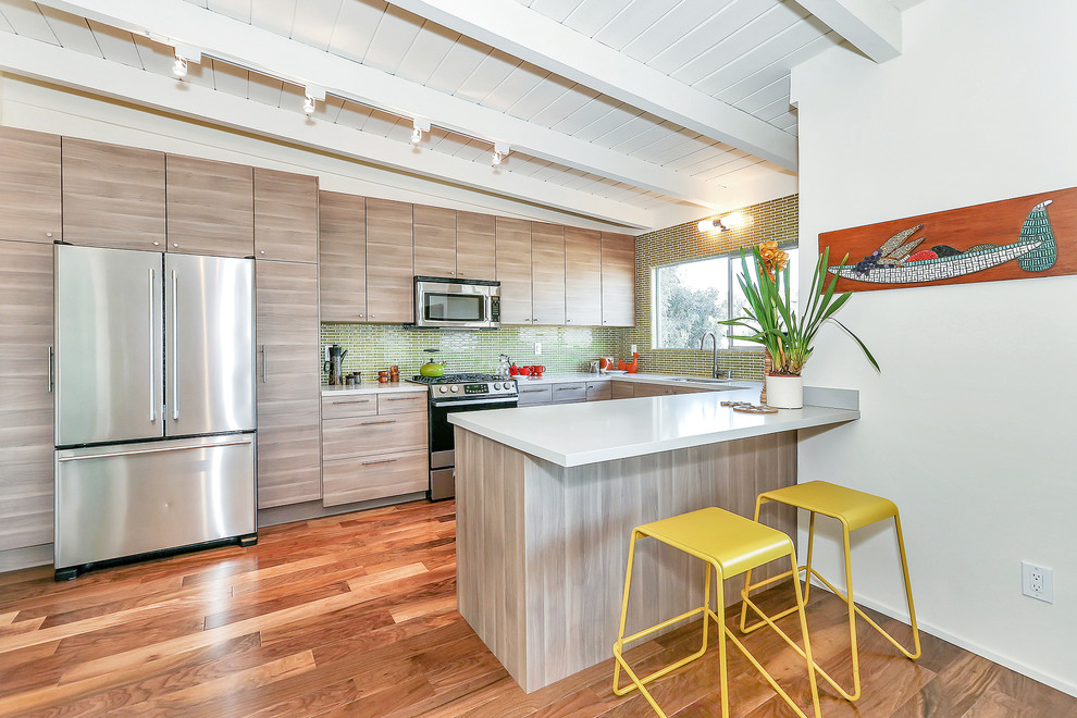 Cette photo montre une cuisine américaine tendance en U et bois clair avec une crédence verte, une crédence en mosaïque, un électroménager en acier inoxydable et un placard à porte plane.