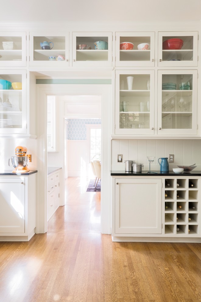 Klassische Küche mit Glasfronten, weißen Schränken, Küchenrückwand in Weiß, braunem Holzboden, braunem Boden und schwarzer Arbeitsplatte in Portland