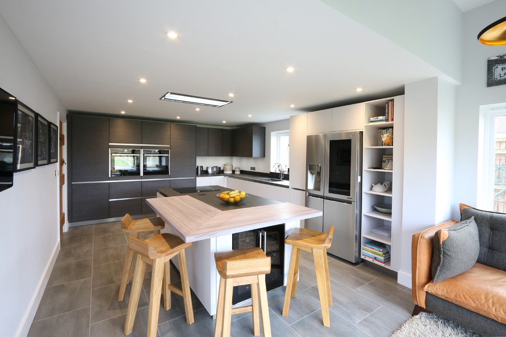 Example of a mid-sized trendy l-shaped gray floor open concept kitchen design in Buckinghamshire with an undermount sink, flat-panel cabinets, stainless steel appliances, an island and black countertops