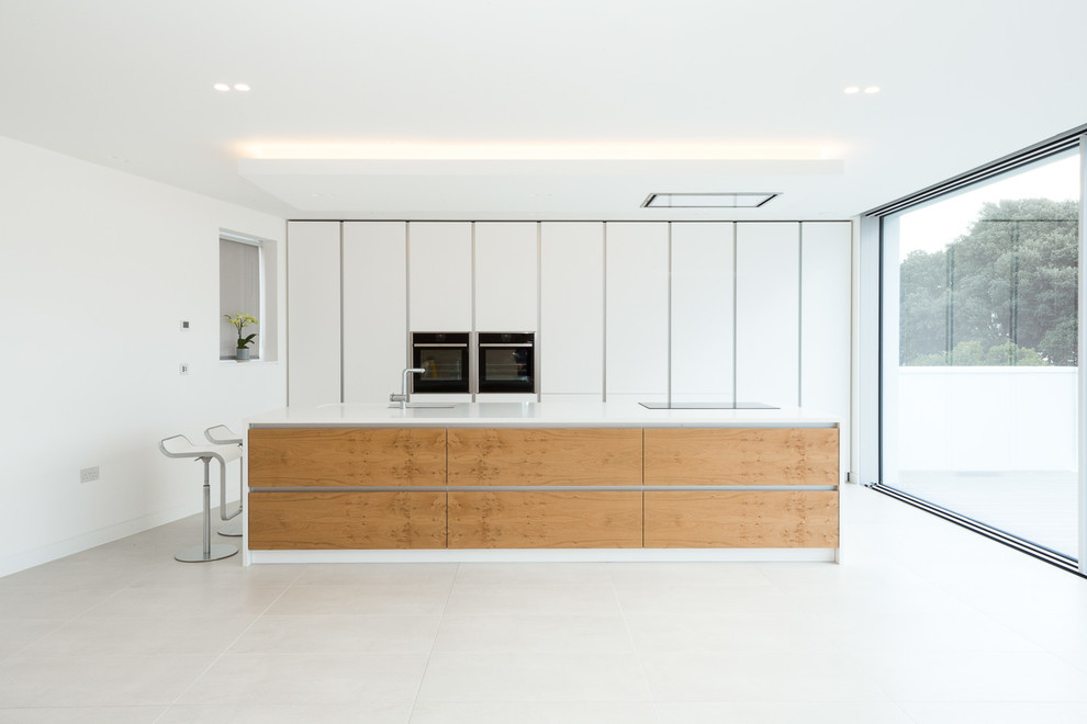 Medium sized contemporary galley kitchen/diner in Dorset with a built-in sink, flat-panel cabinets, white cabinets, composite countertops, stainless steel appliances, porcelain flooring, an island and grey floors.
