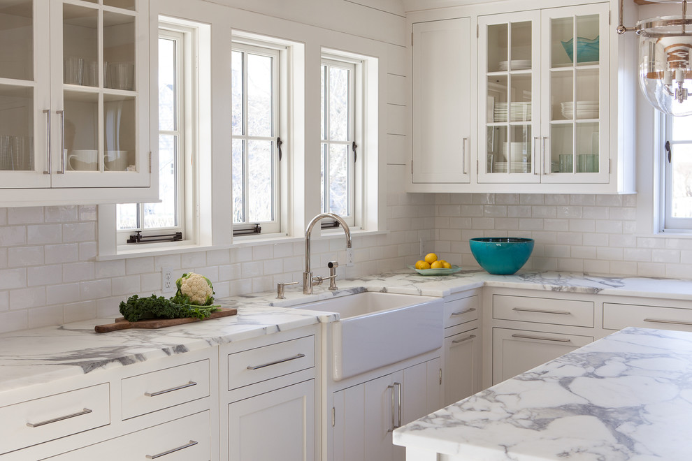 Inspiration for a large coastal u-shaped light wood floor open concept kitchen remodel in Boston with a farmhouse sink, glass-front cabinets, white cabinets, marble countertops, white backsplash, subway tile backsplash, stainless steel appliances and an island