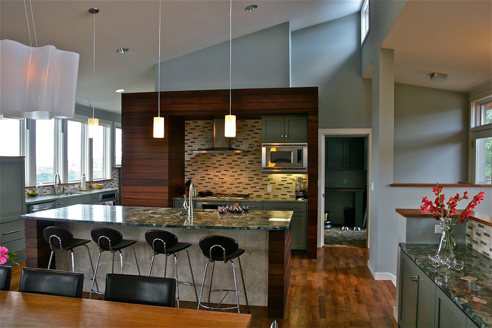 Example of a mid-sized minimalist l-shaped medium tone wood floor open concept kitchen design in Austin with a single-bowl sink, recessed-panel cabinets, green cabinets, granite countertops, beige backsplash, stone tile backsplash and stainless steel appliances