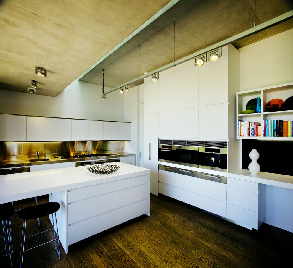 Modelo de cocina minimalista grande con armarios con paneles lisos, puertas de armario blancas, electrodomésticos de acero inoxidable, suelo de madera oscura y una isla