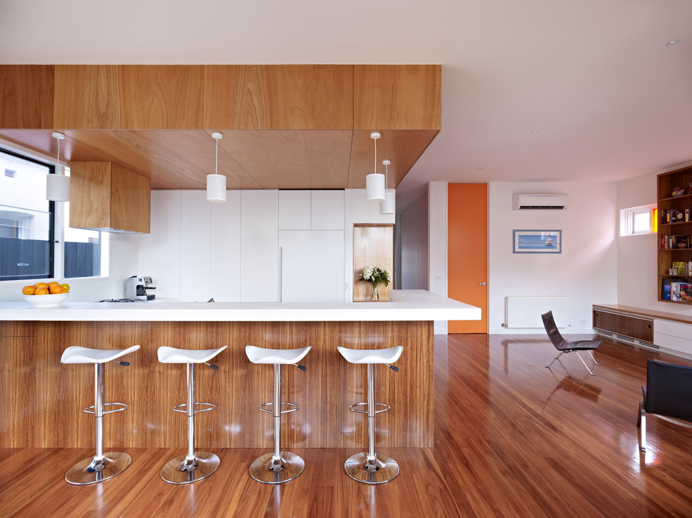 Photo of a medium sized modern u-shaped kitchen/diner in Melbourne with a submerged sink, flat-panel cabinets, white cabinets, engineered stone countertops, white splashback, glass sheet splashback, stainless steel appliances and light hardwood flooring.