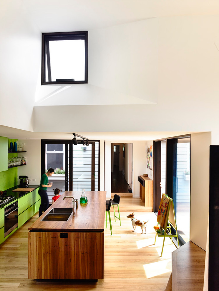 Foto på ett litet funkis kök och matrum, med en dubbel diskho, grönt stänkskydd, rostfria vitvaror, ljust trägolv och en köksö