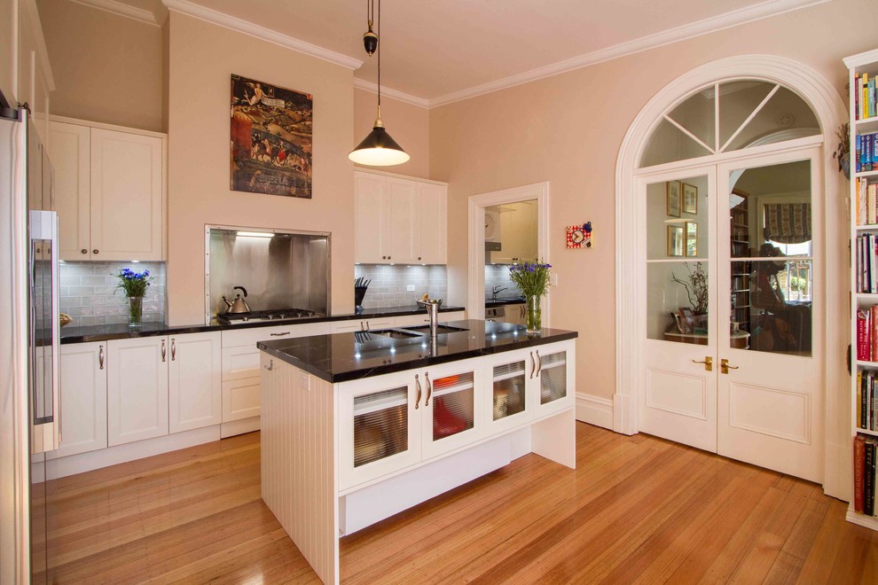 Cette photo montre une cuisine américaine chic en L de taille moyenne avec un placard à porte shaker, un plan de travail en granite, une crédence grise et îlot.