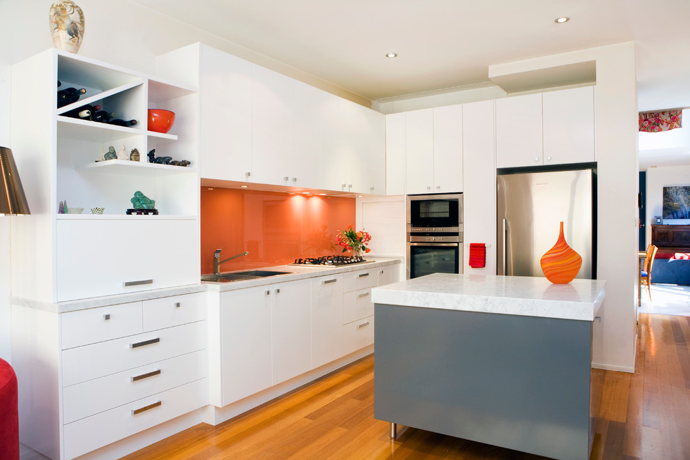 Idéer för mellanstora funkis kök, med en dubbel diskho, släta luckor, vita skåp, marmorbänkskiva, orange stänkskydd, glaspanel som stänkskydd, rostfria vitvaror, ljust trägolv och en köksö