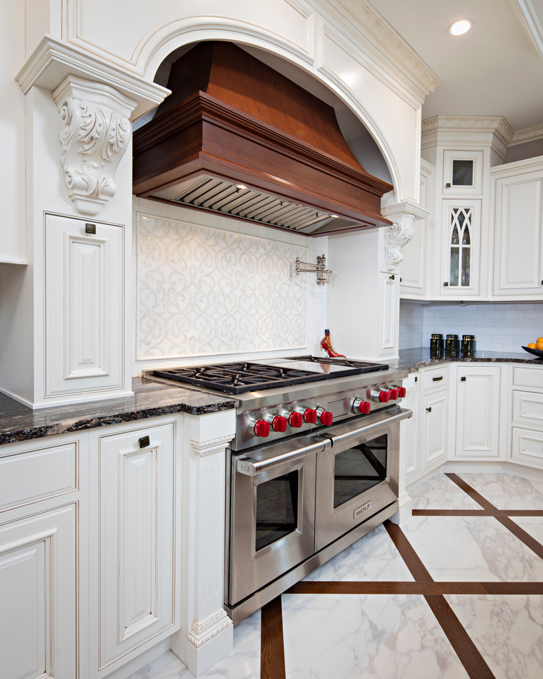 Amerikansk inredning av ett stort kök, med en undermonterad diskho, luckor med upphöjd panel, vita skåp, marmorbänkskiva, vitt stänkskydd, stänkskydd i tunnelbanekakel, rostfria vitvaror, marmorgolv och en köksö