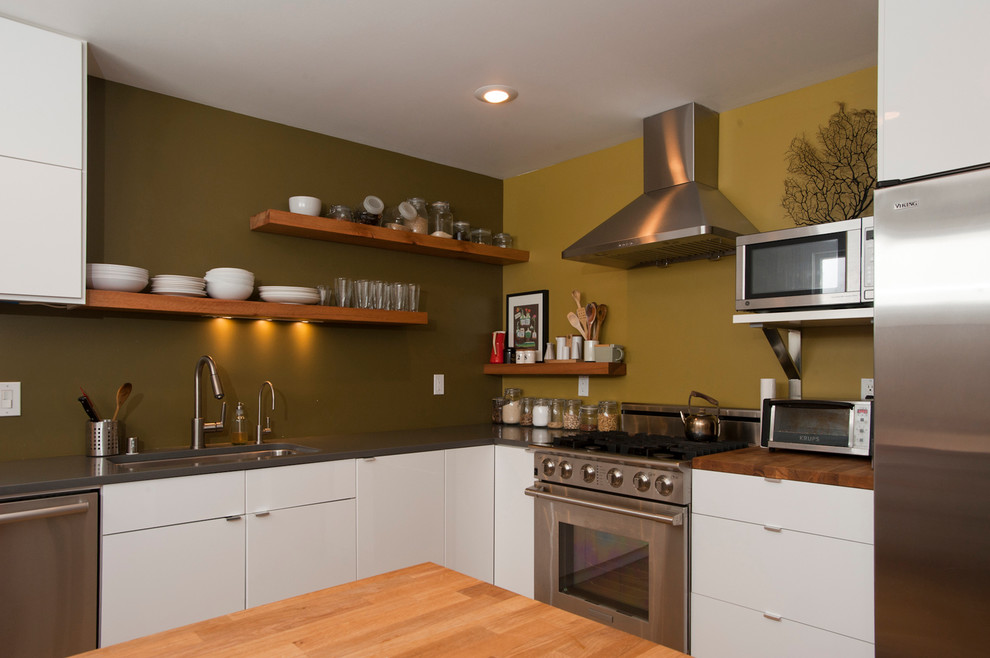 Diseño de cocina minimalista con electrodomésticos de acero inoxidable, encimera de madera, armarios con paneles lisos y puertas de armario blancas