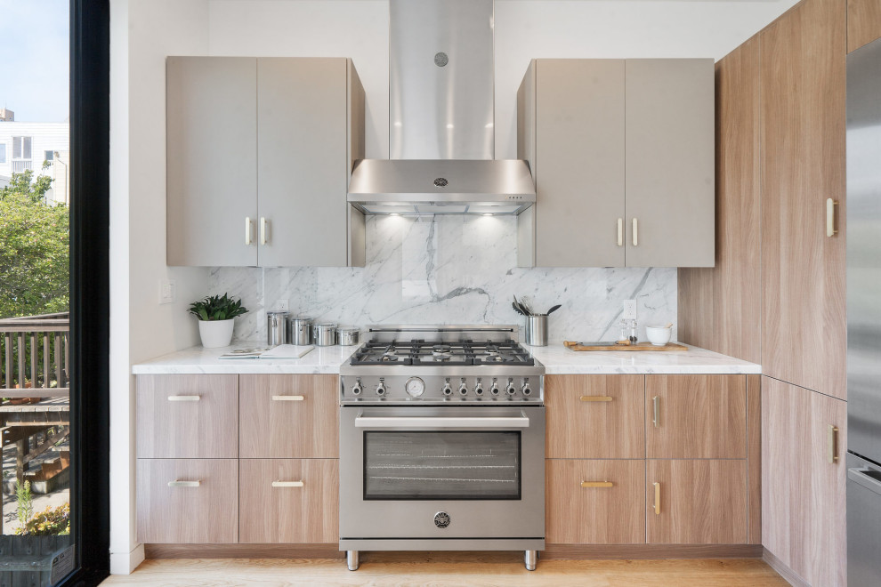 Foto på ett mellanstort funkis vit kök, med en undermonterad diskho, släta luckor, marmorbänkskiva, vitt stänkskydd, stänkskydd i marmor, rostfria vitvaror, mellanmörkt trägolv, en köksö, brunt golv och skåp i ljust trä