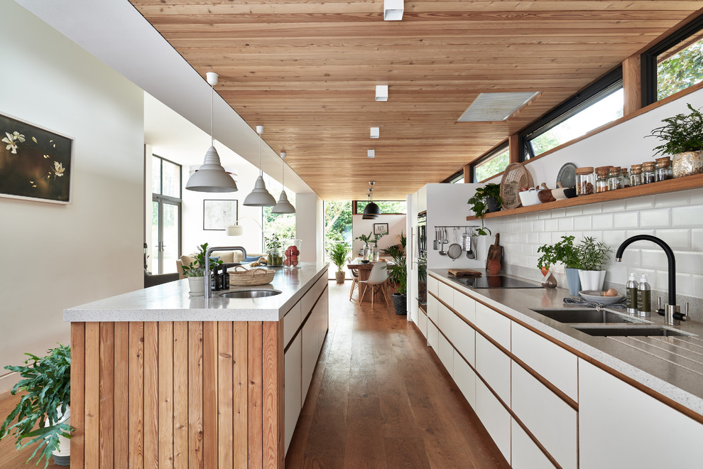 Foto på ett mellanstort funkis grå linjärt kök med öppen planlösning, med släta luckor, vita skåp, bänkskiva i återvunnet glas, vitt stänkskydd, stänkskydd i keramik, mellanmörkt trägolv, en köksö, en dubbel diskho, brunt golv och integrerade vitvaror