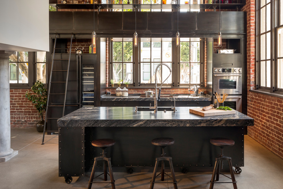 Foto på ett industriellt kök, med svarta skåp, rostfria vitvaror, betonggolv och en köksö