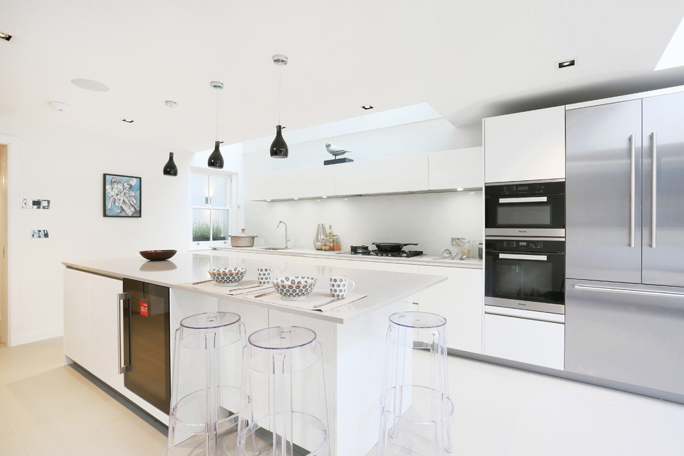 ロンドンにある中くらいなコンテンポラリースタイルのおしゃれなアイランドキッチン (フラットパネル扉のキャビネット、コンクリートカウンター、シングルシンク、白いキャビネット、グレーのキッチンパネル、シルバーの調理設備、白い床) の写真