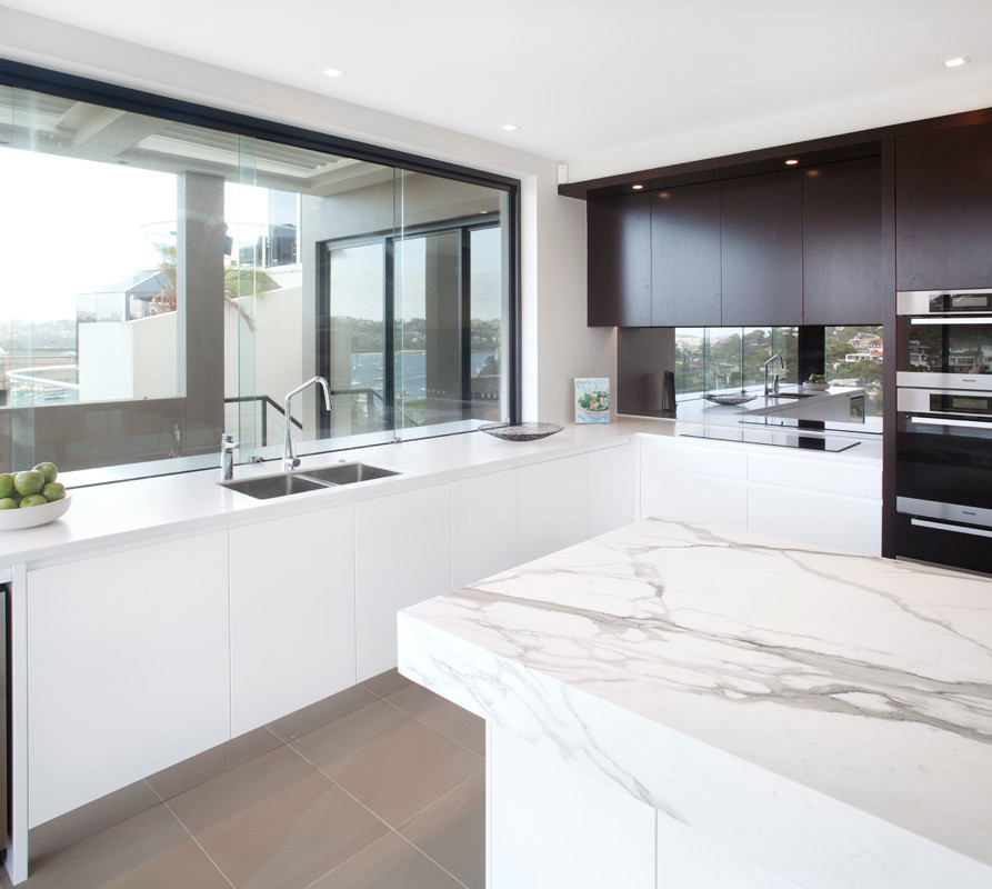 Enclosed kitchen - mid-sized modern l-shaped porcelain tile enclosed kitchen idea in Sydney with an undermount sink, flat-panel cabinets, marble countertops, metallic backsplash, glass sheet backsplash, stainless steel appliances, an island and white cabinets