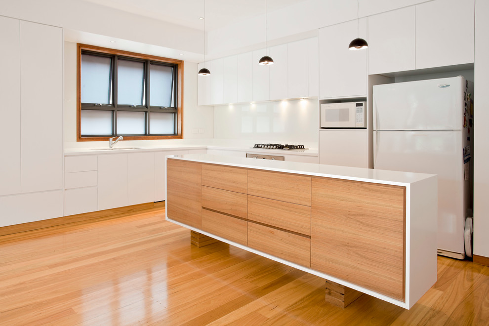 Minimalist l-shaped eat-in kitchen photo in Other with an undermount sink, flat-panel cabinets, white cabinets, solid surface countertops, white backsplash, glass sheet backsplash and white appliances