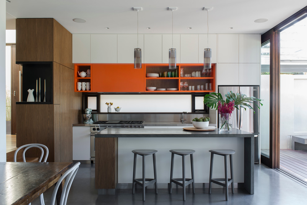 Bild på ett mellanstort funkis kök, med en integrerad diskho, släta luckor, skåp i mellenmörkt trä, granitbänkskiva, stänkskydd med metallisk yta, rostfria vitvaror, en köksö och betonggolv
