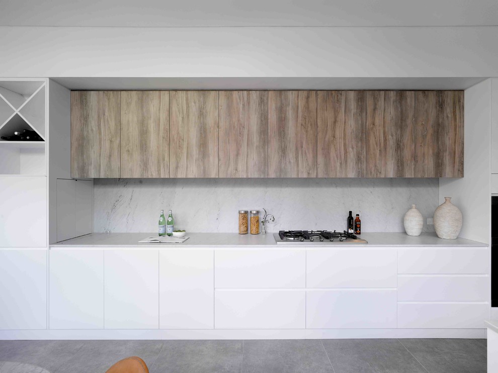 Cette photo montre une cuisine américaine parallèle moderne en bois clair de taille moyenne avec îlot, un placard à porte plane, plan de travail en marbre, une crédence grise, une crédence en marbre, un sol en calcaire, un sol gris et un plan de travail gris.